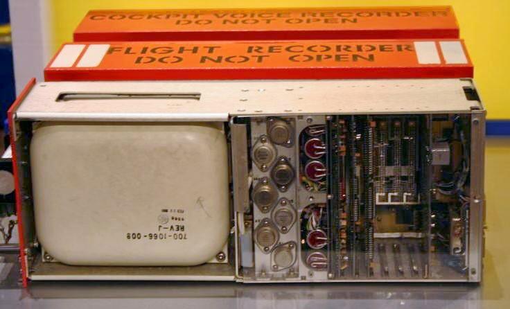 An opened flight data recorder beside its orange casings marked FLIGHT RECORDER DO NOT OPEN and COCKPIT VOICE RECORDER DO NOT OPEN